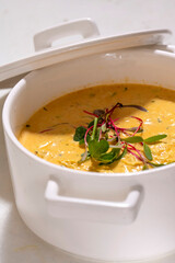 Pumpkin cream soup served with herbs in ceramic pot with lid