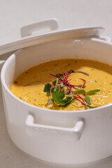 Pumpkin cream soup served with herbs in ceramic pot with lid