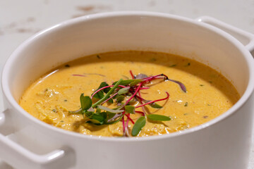 Pumpkin cream soup served with herbs in ceramic pot with lid