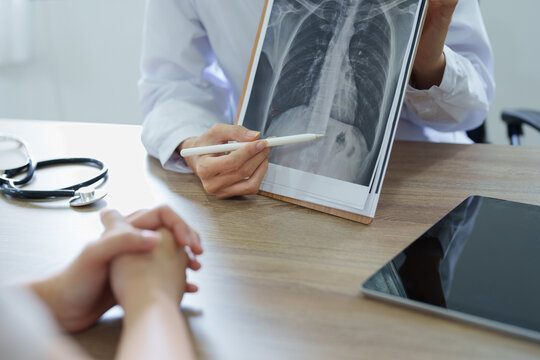 An Asian female doctor points to a patient x-ray film to explain the patient's treatment process