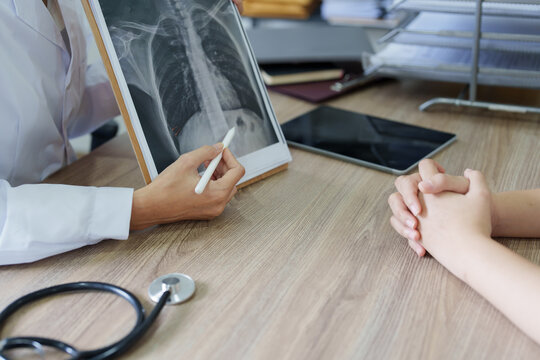 An Asian female doctor points to a patient x-ray film to explain the patient's treatment process