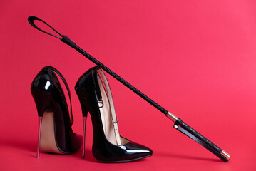 Black shiny high heel shoes and a whip on a red background