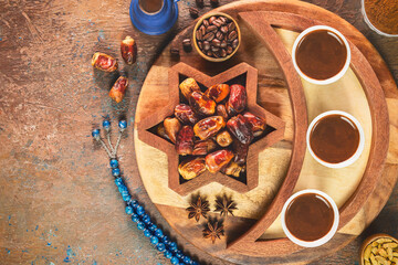 Turkish coffee cups placed with roasted coffee beans, fresh dates and rosary beads on rustic background. Top view with copy space.