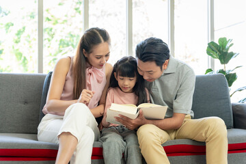 Obraz premium Asian family portrait Parents and daughters are happily reading together on the sofa in the house together.