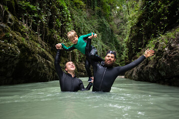 a man with a child in wetsuits in a canyon with a river