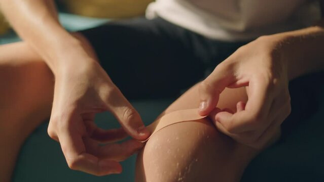 Teenage boy applying medical adhesive plaster on his knee. First aid after injury. Cuts, abrasions and lightly bleeding wounds while doing sports concept.