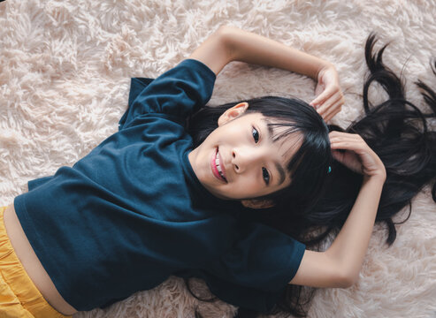 Cute 7-9 kid girl lying smiling playing on floor carpet smiling looking at camera