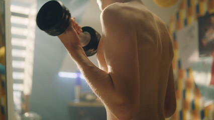 Muscular schoolboy doing dumbbells curls in his room. Closeup of his arms and muscular abs. Weight...