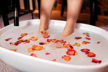 female feet soaking in a bucket with a water and flower petals bath for a pedicure, concept of wellness and body care © Raul Mellado