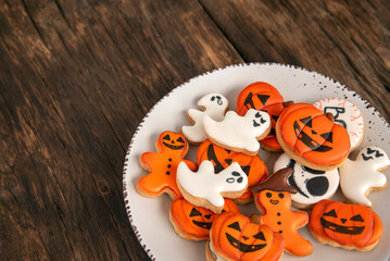 Obraz na płótnie Canvas Orange Halloween cookies in the shape of pumpkin ghosts in big plate on a wooden table. Place for text. Top view