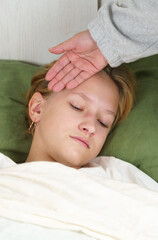 Mom touches her hand to the forehead of a sick daughter lying on the bed.