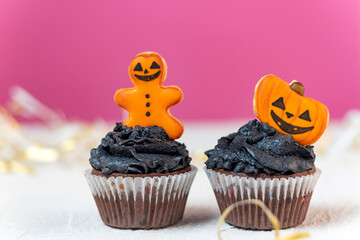 Halloween cupcakes with pumpkins and gingerbread man. Two cupcakes for the celebration of Halloween on pink background