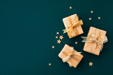 Christmas gifts or presents with golden bow ribbon and star confetti on green background top view....