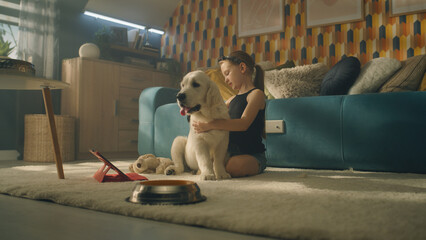 Young girl playing with dog, smiling and laughing, sitting together on mild carpet, spending...