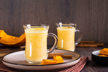 Pumpkin latte in glasses and pieces of pumpkin in a bowl on a wooden table. Homemade autumn drinks
