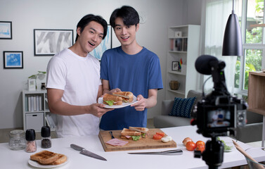Young Asian male couple blogger influencer vlogger shooting video in kitchen. LGBT  gay couple live- streaming cooking class from home.