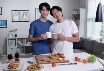 Portrait of romantic Asian gay couple cooking on kitchen and looking at camera. Lgbt men couple are...
