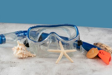 Blue snorkel mask with shells on the sand with blue background