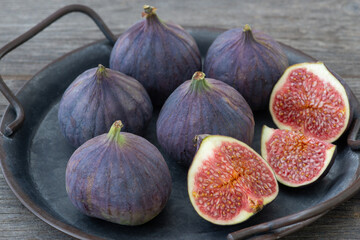 fresh figs on an iron plate, wooden table, slices and whole fruits, rustic