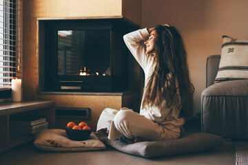 Cozy home. Young woman relaxing near the fireplace.