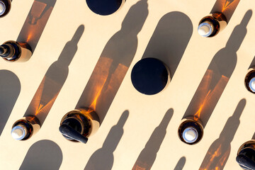 Pattern made with brown glass bottle of cosmetic products and strong shadow on beige background, as a backdrop or texture. Creative layout for your design