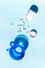 Pills and glass of water on blue background. Medicine, healthcare concept