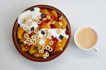 Fondo con textura y detalle de bol de macedonia, cereales, yogur y chocolate, junto a una taza de café