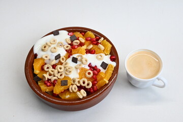 Fondo con textura y detalle de bol de macedonia con yogur, cereales y trozos de chocolate, junto a una taza de café