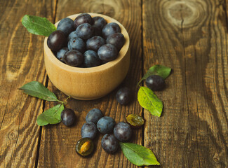 Blue plum in a bowl on a wooden table. Fruit background with copy space.