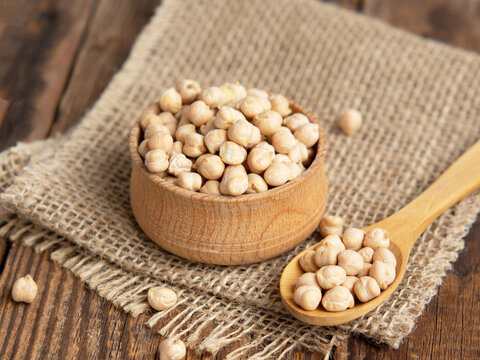 Wooden bowl and wooden spoon full of chickpeas on a wooden background.