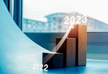 Shining rise up arrow on wood blocks chart steps as a graph from year 2022 to 2023 on blue...