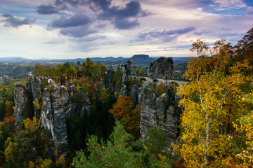 Amazing autumn landscape in Saxon Switzerland National Park. View of The Bastei is a rock formation, exposed sandstone rocks and forest hills at sunset. Germany. Saxony.