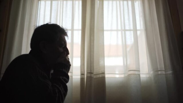 Mature man by a window and constantly coughing from the respiratory disease he has.