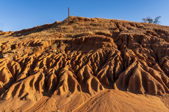 A dry river bed with high eroded sides of red dirt