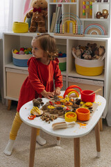 A little girl playing with autumn natural materials and make a tree with colored rice. Child filled the leaves with yellow and orange rice.  Montessori material. Sensory play and fall nature crafts