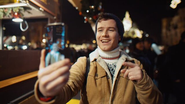 young Blogger record himself on phone at night on a busy street on Christmas and new year under the Christmas tree at the New Year's fair in Europe
