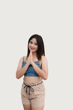 A beautiful Asian girl poses for the camera with both hands together, doing a praying position as she gestures to ask for a favor. Studio shot isolated on white background.