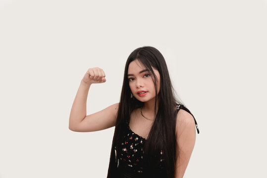 An Asian lady doing a strong or tough hand gesture as she holds her arm and fist up and flexes her biceps. Studio shot isolated on a white background.