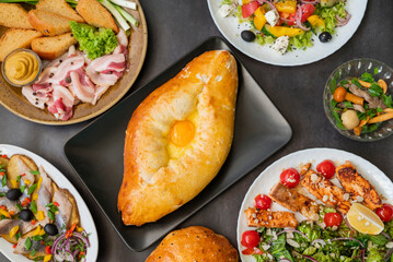 top view of khachapuri dish with cheese and egg in Adjarian with Caesar and Greek salads with potatoes and herring on the table