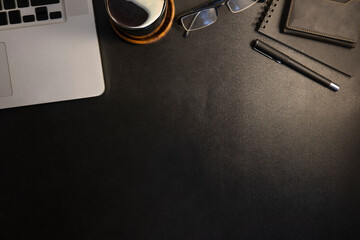 Laptop computer, coffee cup, glasses and notepad on black leather background.