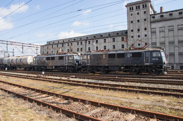 Obraz premium Railroad tracks and a train against the backdrop of an abandoned and destroyed industrial building. Day.