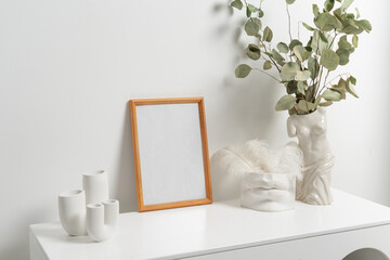Wooden vertical frame with white vase of eucaliptus leaves over white wall