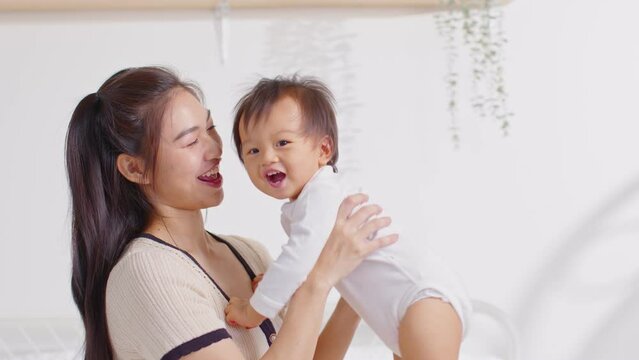 Asian mom holding her baby newborn in hand laughing sweet and lovely. Good moment of Happy mother and infant baby looking together smile with love. Wellness family. Mother and baby newborn Concept