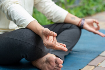 Close up woman mudra hand gesture doing yoga relaxing in lotus position sitting on mat. outdoors....