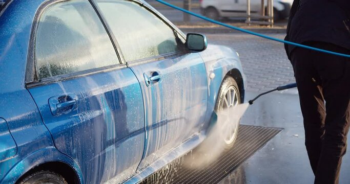Closeup of modern vehicle washed by anonymous person with high pressure water. A very dirty car is cleaned with a jet of clean water
