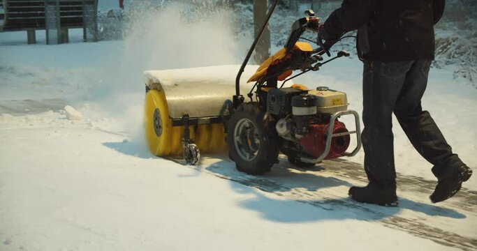 Man working with snow blower. A person cleans pavement from snow with blower. Heavy precipitation and snow piles on the pavement.