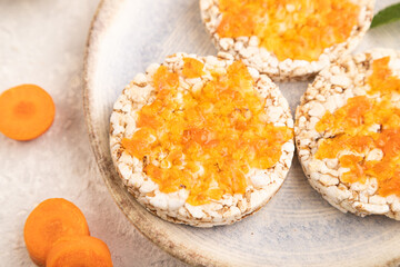 Carrot jam with puffed rice cakes on gray concrete. Side view, selective focus.