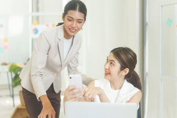 Obraz premium Two business woman wearing white suit using laptop and smartphone for online digital content in office
