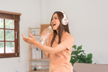 Fototapeta na wymiar Relaxation concept, Young woman wear headphone listening music and hold water bottle to singing