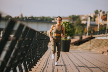 Active young beautiful woman running on the promenade along the riverside